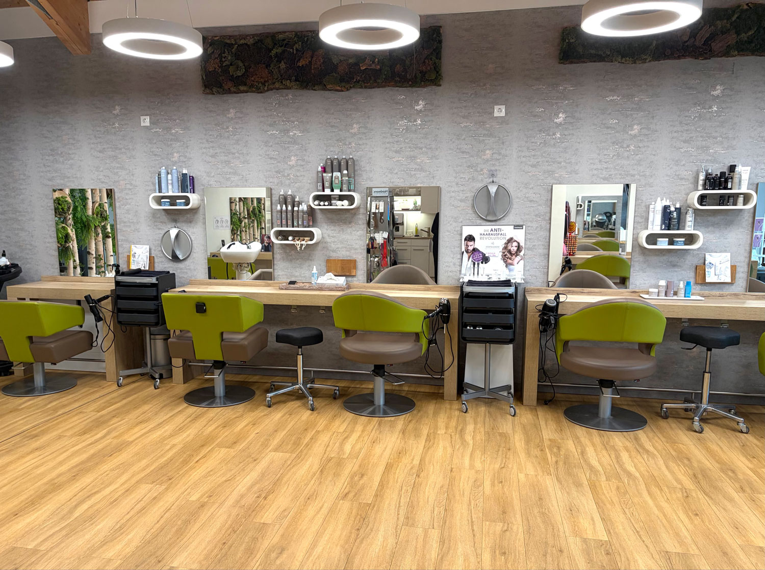 Bedienplätze in Reihe mit Spiegeln, Pflegeprodukten und grünen Friseurstühlen